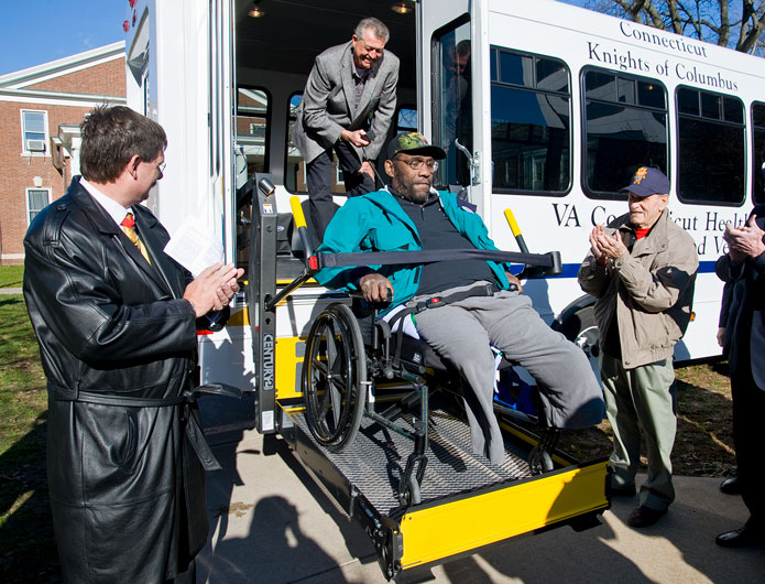Volunteer Knights help  a veteran Knight exit a medical transport vehicle