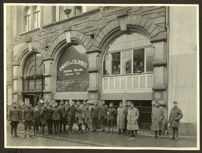 Military men pose outside of a building with the sign Everybody Welcome, Everything Free